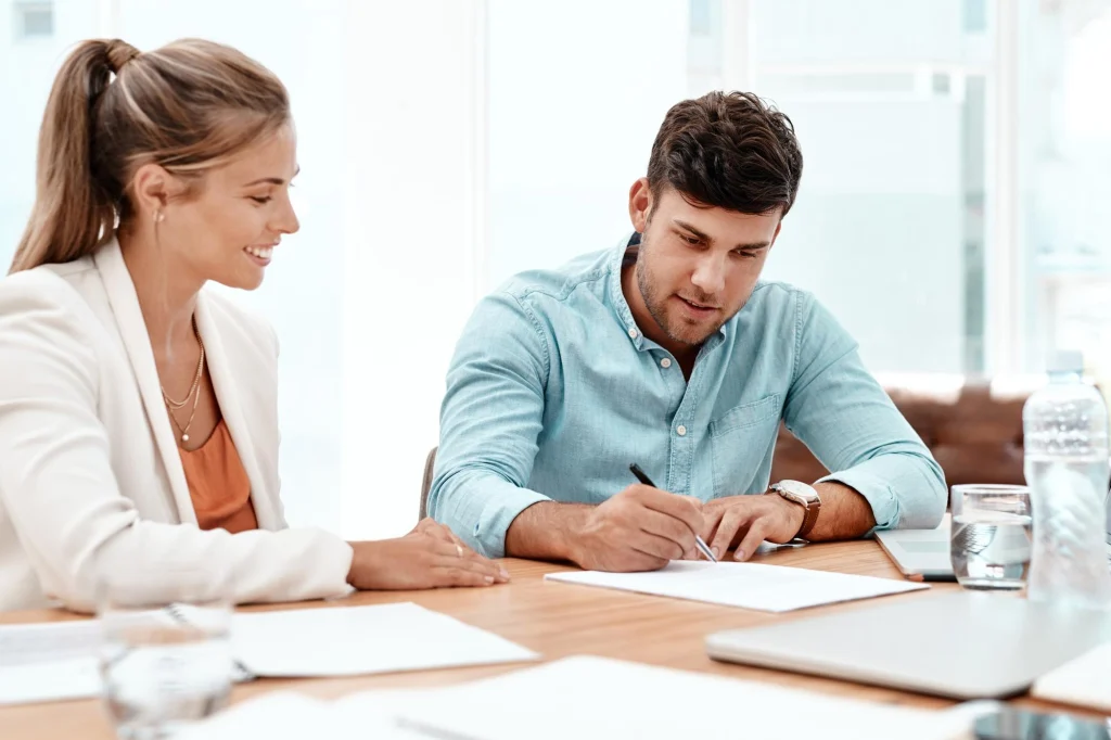 Frau und Mann gehen gemeinsam Unterlagen am Bürotisch durch, der Mann notiert mit einem Stift